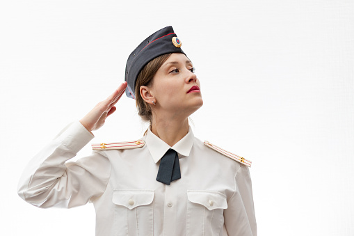 A beautiful young female Russian police officer in dress uniform and a white shirt on a white background salutes the commander. Selective focus. Portrait