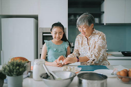 Asian Chinese Senior woman showing and teaching granddaughter preparing Chinese dumpling in kitchen during weekend leisure time