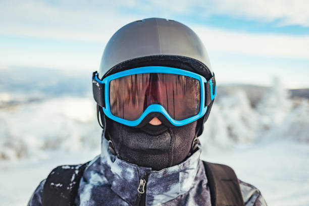 Man wearing a sports suit helmet and ski goggles A skier up close on a snowy mountain slope, wearing a sports suit helmet and ski goggles over the blue sky copy space face guard sport stock pictures, royalty-free photos & images
