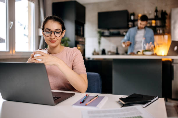 istock Young beautiful woman working from home while her husband is in the background 1373269103