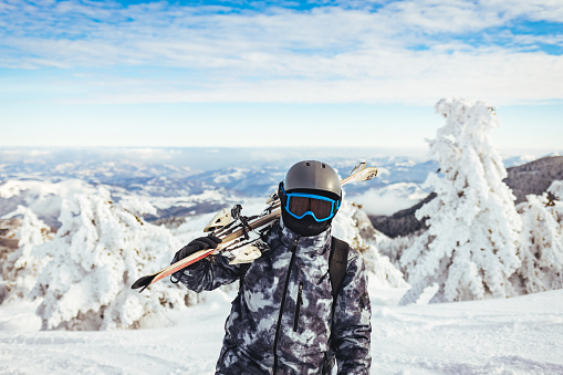 Portrait of a skier in the ski resort on the background of mountains and blue sky. Ski goggles of a man with the reflection of snowed mountains. wearing ski glasses. Winter Sports