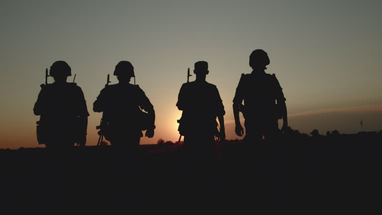 Silhouettes of snipers in ammunition going to homeland after battle at sunset.