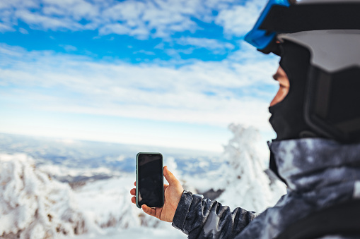 A skier holding a smartphone with a snow mountain in the background.