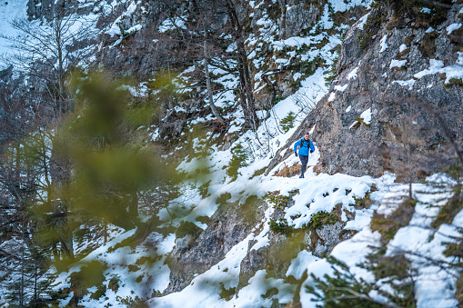 A Caucasian male hiker in his 50's wearing a blue down jacket running on the trail of snowy mountains.