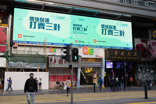Hong Kong - February 28, 2022 : People walk past a government advertisement encouraging the public to take all three doses of COVID-19 Vaccine in Hong Kong.