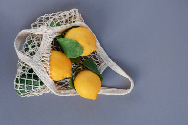 istock Lemon fruits with leaves in mesh bag on gray background. Zero waste concept. Top view, flat lay 1373281017