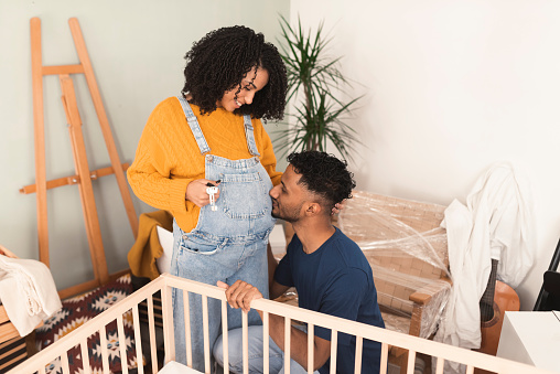 Happy multiracial couple expecting a baby and preparing a crib while moving into the new home