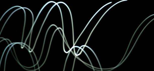 istock Closeup of White neon Curved Wave pattern abstract flowing in a isolated black background with copy space made using  photography technique called Long exposure. 1373281767
