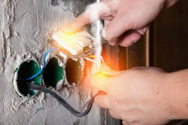 A man holds on to electrical wires and an electrical switch. Electric shock, flash of fire and smoke. Safety