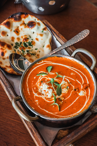 Indian Creamy butter chicken curry with paratha bread served in copper bowl