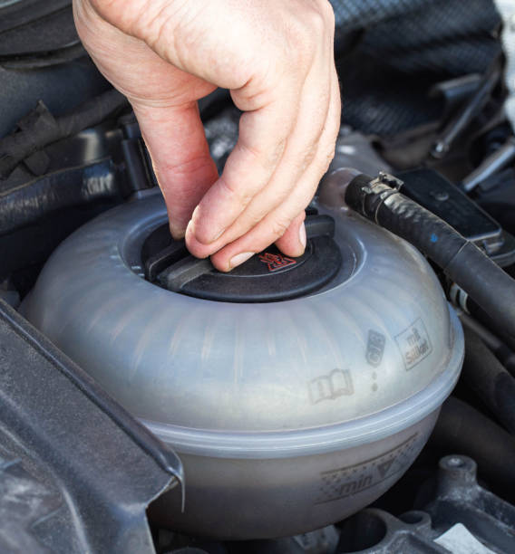 un hombre desenrosca la tapa del tanque de expansión de un automóvil con refrigerante, de cerca. problema de sobrecalentamiento del motor, esclusa de aire - airlock fotografías e imágenes de stock