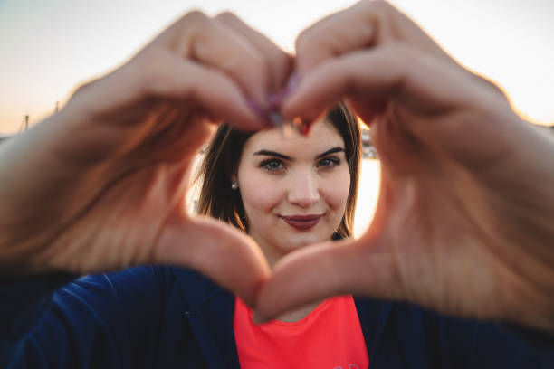 Happy curvy woman framing her face with an heart shape with fingers - self acceptance and self esteem concept stock photo