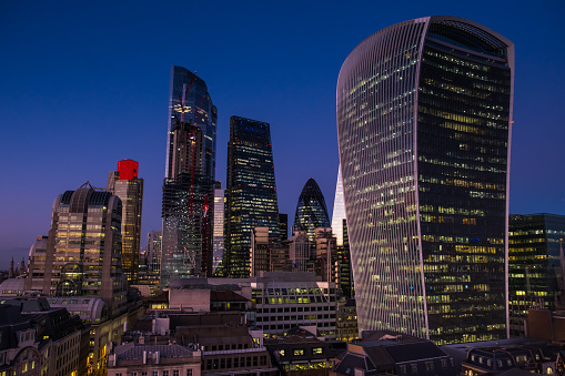 The iconic curves of The Gherkin framed by the illuminated office buildings of the City of London’s Square Mile Financial District, UK.