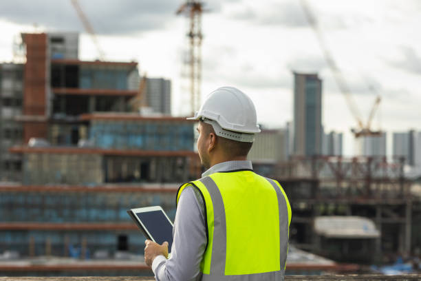 istock Asian engineer handsome man or architect use tablet with white safety helmet in city construction site . Standing on rooftop building construction at capital. 1373287393