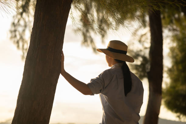 istock Young asian woman with straw hat standing alone on beach looking at sunset seashore. Chilling in holiday weekend summertime. Traveler Female walking around the beach with the sunlight 1373287513