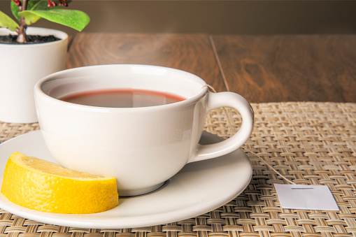 A cup of tea with lemon on a saucer.