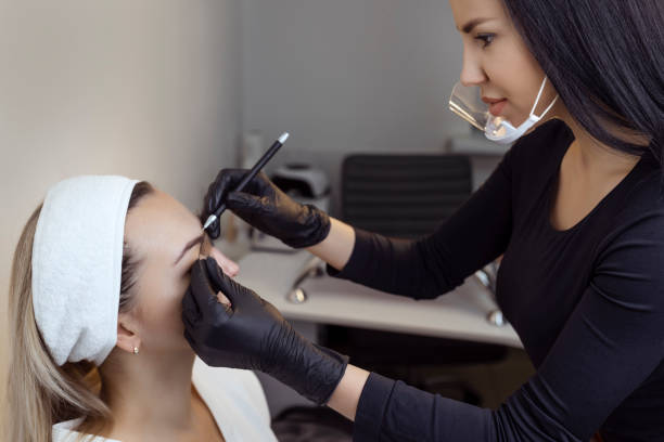 The hand of a make-up artist in black gloves applies a contour to the eyebrow with a black eyebrow pen. Professional stylish permanent makeup, eyebrow tinting. Close. The hand of a make-up artist in black gloves applies a contour to the eyebrow with a black eyebrow pen. Professional stylish permanent makeup, eyebrow tinting. hand tinted stock pictures, royalty-free photos & images