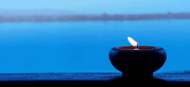 Candle light fire lamp nearby abstract background river during sunset or sunrise in countryside. Melting candlestick in evening twilight. Religion abstract concept.