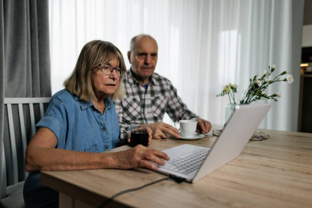 concerned senior couple reading news in internet at home - common serious couple men imagens e fotografias de stock