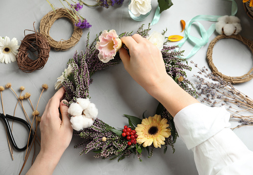 Florist making beautiful autumnal wreath with heather flowers at light grey table, top view