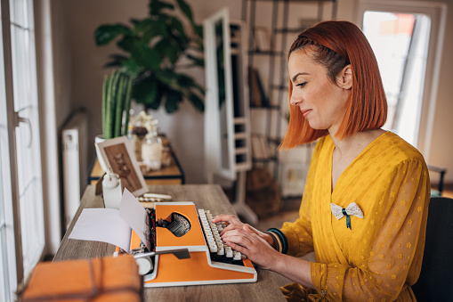 One woman, beautiful female redhead writer sitting at the desk at home and typing on typewriter.