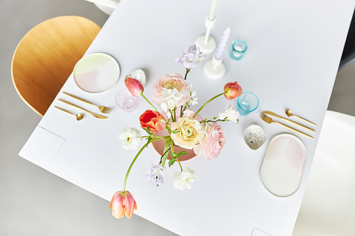 A modern spring bouquet with freesias, ranunculus and tulips in a beautiful vase on a white dining table