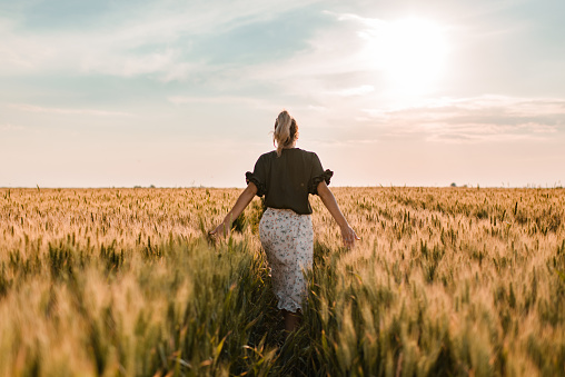 Young woman touching crops in field on a sunset.
