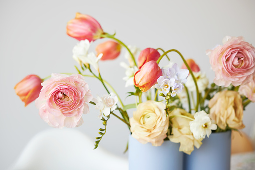 A modern spring bouquet of freesias, ranunculus and tulips in a beautiful vase on a dining table