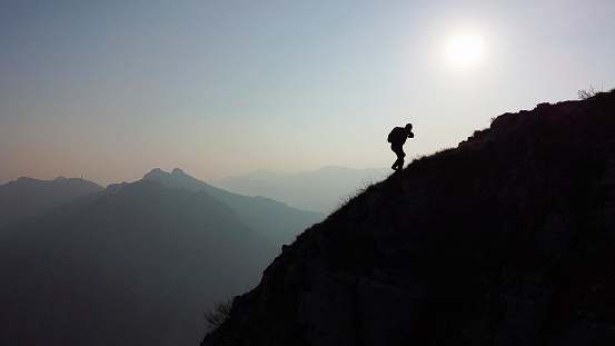 Hiker climbs a mountain ridge, sun and backlight