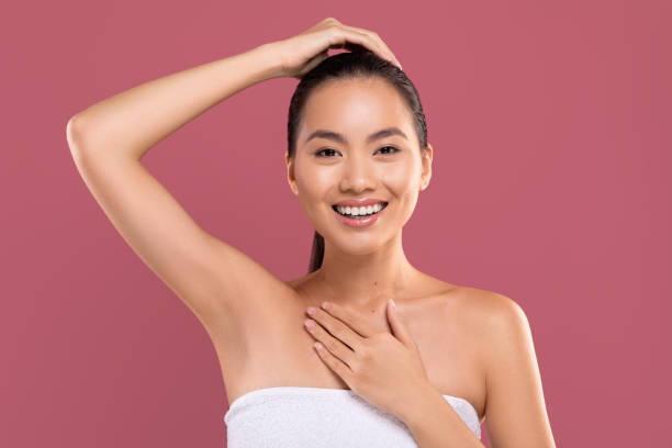 Cheerful japanese woman showing her clean and hairless armpit Cheerful attractive young japanese woman wrapped in white towel raising hand up and smiling, showing her clean and hairless armpit, posing over purple studio background, copy space underarm stock pictures, royalty-free photos & images