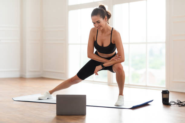 istock Young black woman doing side lunges on mat using laptop 1373301011