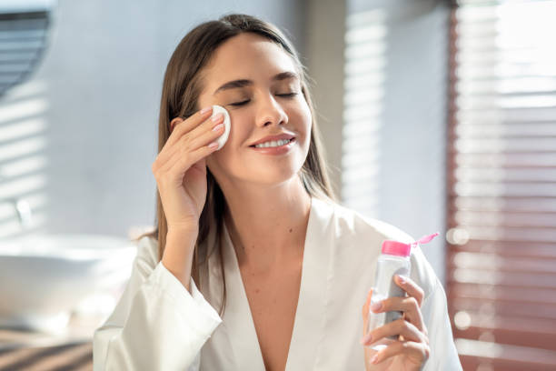 beautiful smiling woman cleansing skin with micellar water and cotton pad - gezicht wassen stockfoto's en -beelden