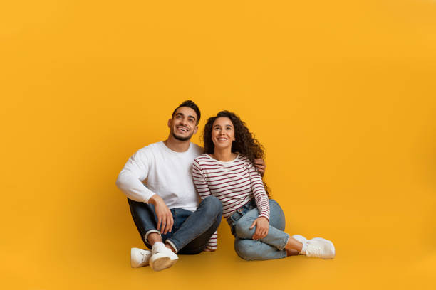 istock Dreamy Young Arab Couple Sitting On Floor And Looking At Copy Space 1373301214