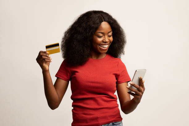 compras en línea. alegre joven mujer negra usando teléfono inteligente y tarjeta de crédito - greeting card holding women credit card fotografías e imágenes de stock