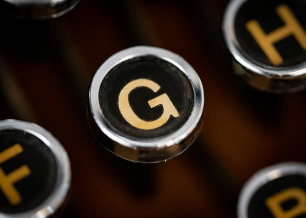 Retro vintage typewriter circular round key closeup with gold coloured letter G on black background.