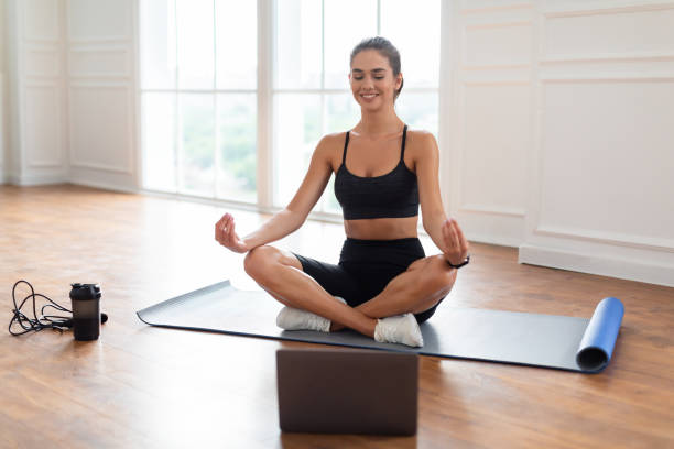 istock Young woman meditating in lotus position on mat with pc 1373302620