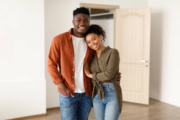 loving black couple embracing smiling to camera in new house - couple black imagens e fotografias de stock