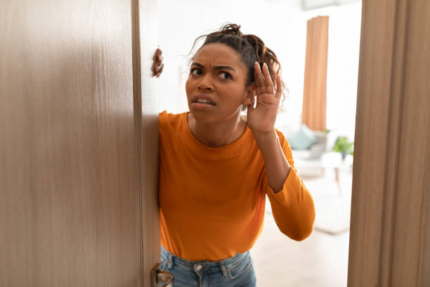 Displeased Black Lady Listening Standing In Opened Door At Home Displeased Black Lady Listening Holding Hand Near Ear Standing In Opened Door Having Problem With Soundproof At Home. Concerned Woman Hearing Something Openind Door Of Her House eavesdropping stock pictures, royalty-free photos & images