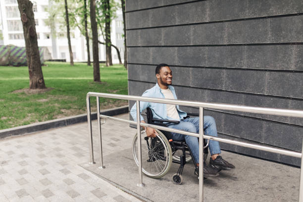 istock Accessible environment for people with special needs concept. Positive young black man in wheelchair using ramp outdoors 1373304498