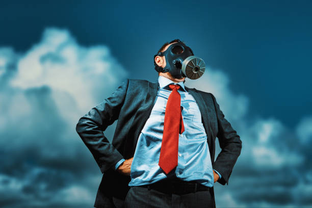 Be prepared: businessman wears a military gas mask as he stands confidently against the sky Man in a suit and tie looks determined as he stands, hands on hips, with a gas mask incongruously on his face. calm before the storm stock pictures, royalty-free photos & images