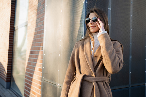 Portrait of stylishly dressed woman in sunglasses near building wall