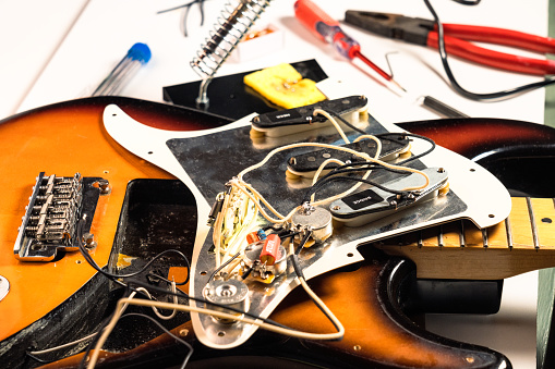 A guitar opened up to replace the three single-coil pickups, seen upside down on the pickgard, along with the guitar's controls and tools in the background.
