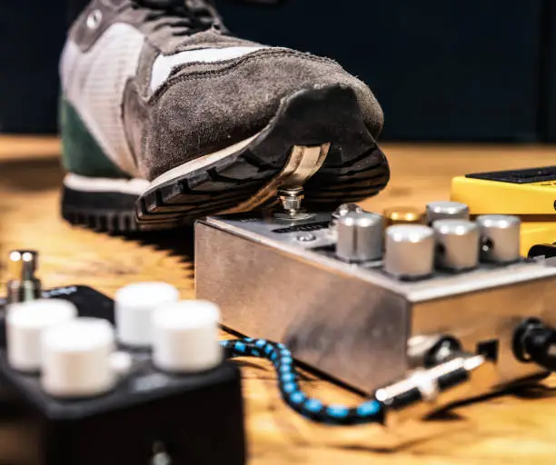 A guitarist switching on a compression pedal while playing.