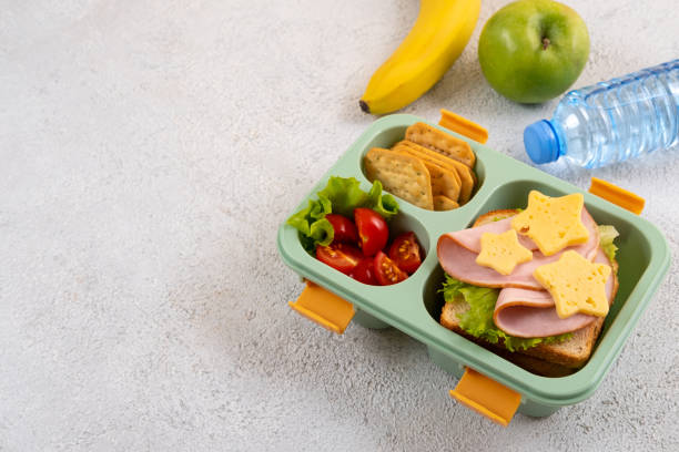 gesunde schulbrotbox mit sandwich und salat auf dem tisch. banane, apfel und eine flasche wasser. zurück zur schule - lunch box lunch sandwich green stock-fotos und bilder