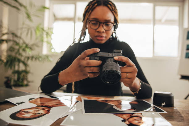 Photographer holding a dslr camera in her home office. Self-employed photographer working with photographs at her desk. Creative female freelancer working on a new photographic project.