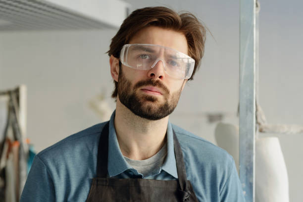 istock Young serious workman in apron and protective eyewear 1373344498
