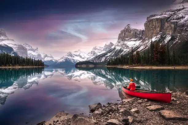 Photo of Female traveler in winter coat rowing a red canoe in Spirit Island on Maligne Lake at the sunset