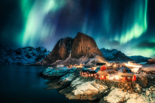 aurores boréales, aurores boréales au-dessus de la montagne avec village de pêcheurs sur la côte à hamnoy, îles lofoten - travel destinations hill landscape house photos et images de collection