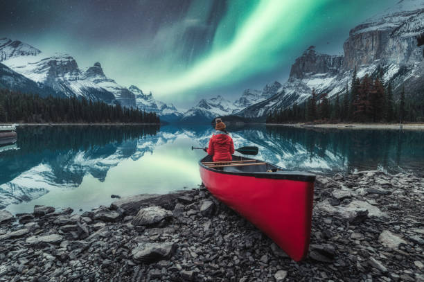 aurores boréales au-dessus de l’île spirit avec une voyageuse assise sur un canot rouge sur le lac maligne au parc national jasper - jasper alberta photos et images de collection