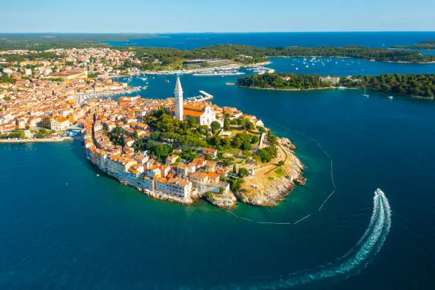 Surroundings of Rovinj and tower of St. Euphemia church. Croatian town buildings near forests and Adrianic sea at bright sunlight. Aerial panorama